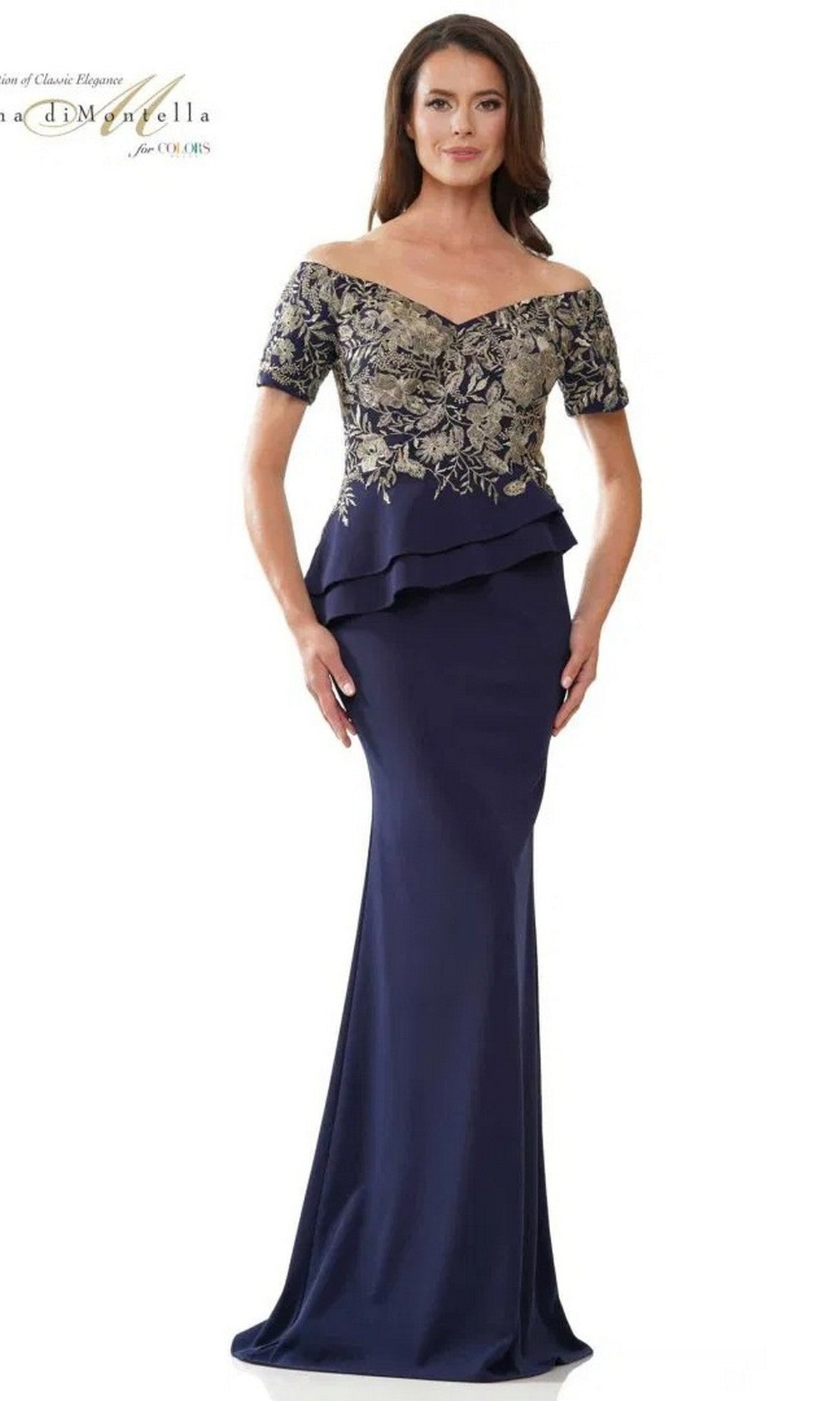 A woman wears the Rina Di Montella RD2918 long formal dress in navy, featuring an off-shoulder fitted bodice, gold floral embroidery, short sleeves, and a peplum waist detail.